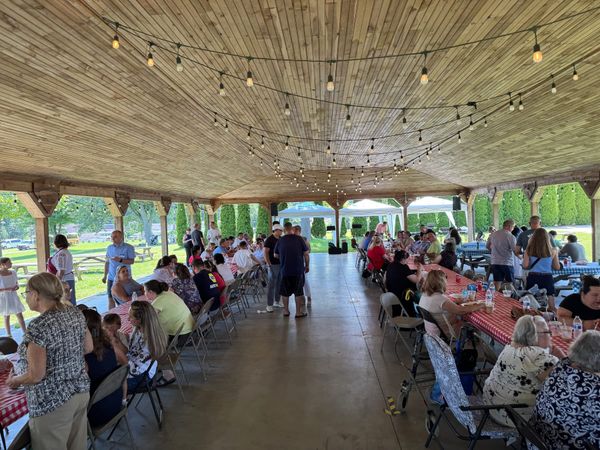 Church family eating together at long tables under a large park pavilion
