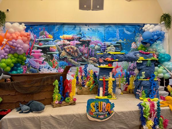 The stage decorated with an ocean mural, coral, and colorful balloons