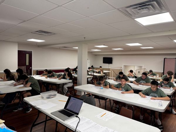 Students writing their Sunday School exam at long tables