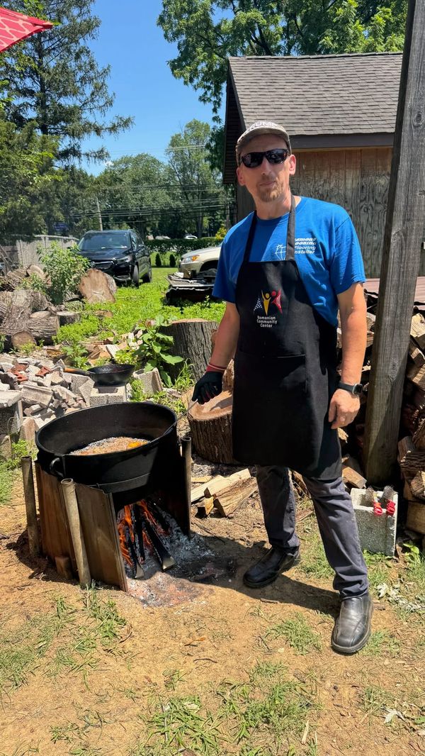 A man in an apron cooking in a cauldron over a wood fire